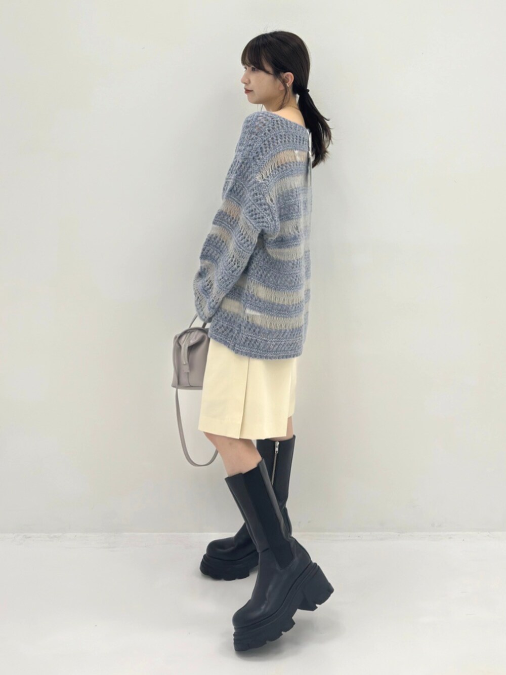 ブラック系のブーツ、ブルー系のニット/セーター、グレー系のハンドバッグを着用したレディースの秋コーディネートの2枚目の写真