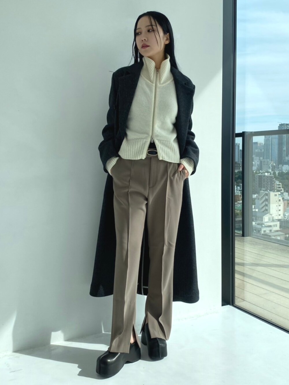 グレー系のチェスターコート、ホワイト系のニット/セーター、グレー系のスラックスを着用したレディースの秋コーディネートの2枚目の写真