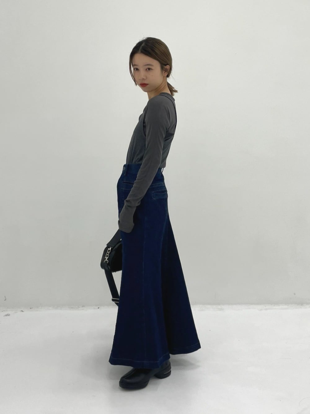 ブラック系のショルダーバッグ、グレー系のTシャツ/カットソー、ブルー系のスカートを着用したレディースの秋コーディネートの2枚目の写真