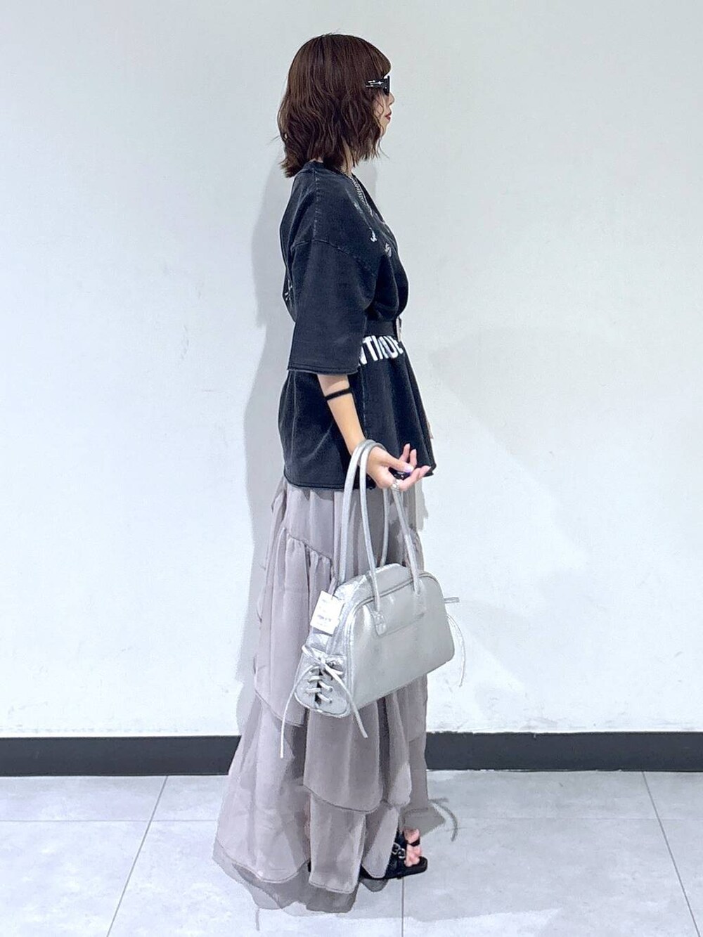 グレー系のスカート、シルバー系のショルダーバッグ、ブラック系のサンダルを着用したレディースの夏コーディネートの3枚目の写真