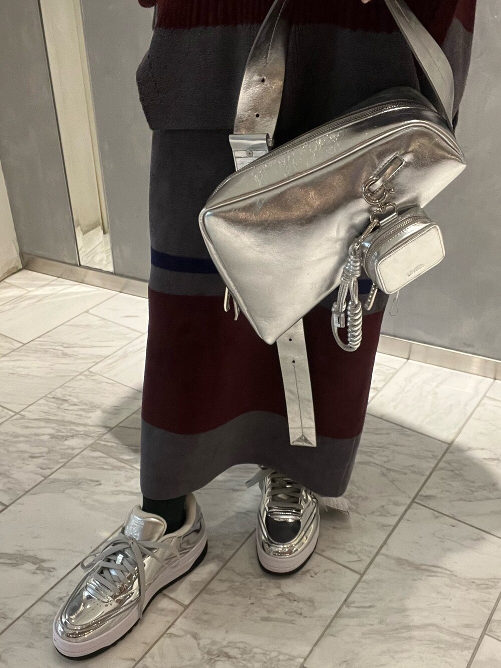 シルバー系のスニーカー、シルバー系のショルダーバッグ、グレー系のニット/セーターを着用したレディースの冬コーディネートの6枚目の写真