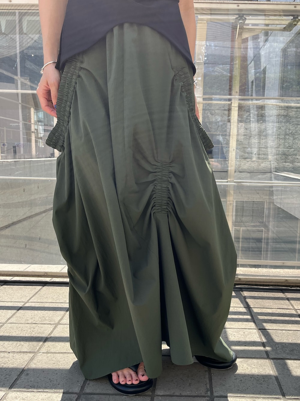 ブラック系のTシャツ/カットソー、グリーン系のスカート、ブラック系のサンダルを着用したレディースの春コーディネートの7枚目の写真