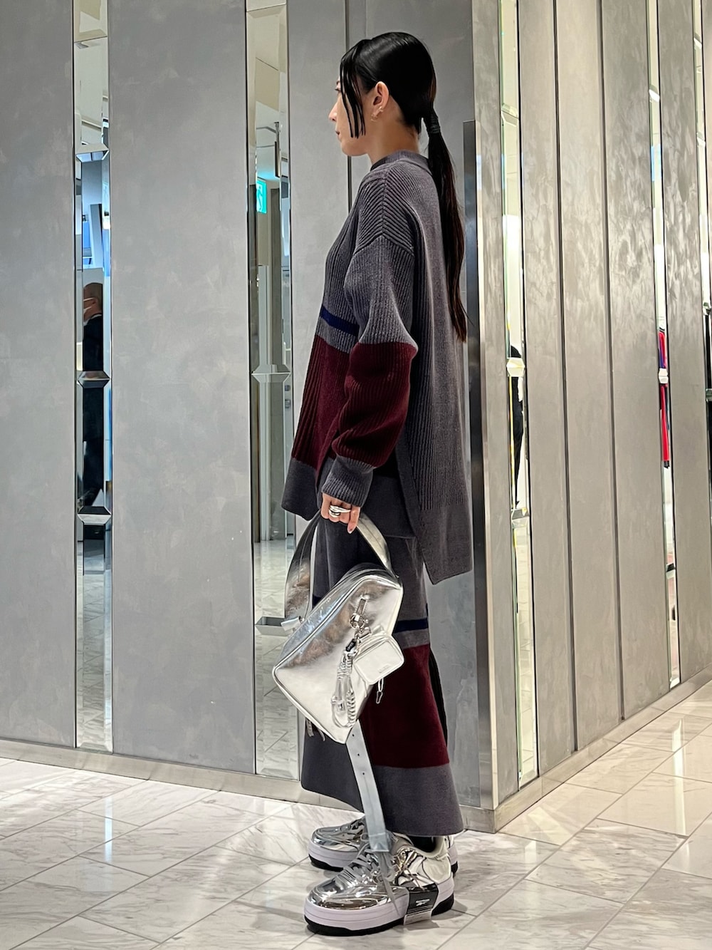 シルバー系のスニーカー、シルバー系のショルダーバッグ、グレー系のニット/セーターを着用したレディースの冬コーディネートの2枚目の写真