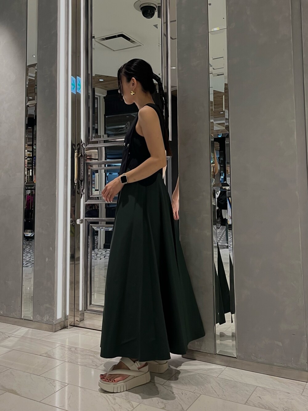 グリーン系のスカート、ブラック系のタンクトップ、ゴールド系のピアス（両耳用）を着用したレディースの春コーディネートの2枚目の写真