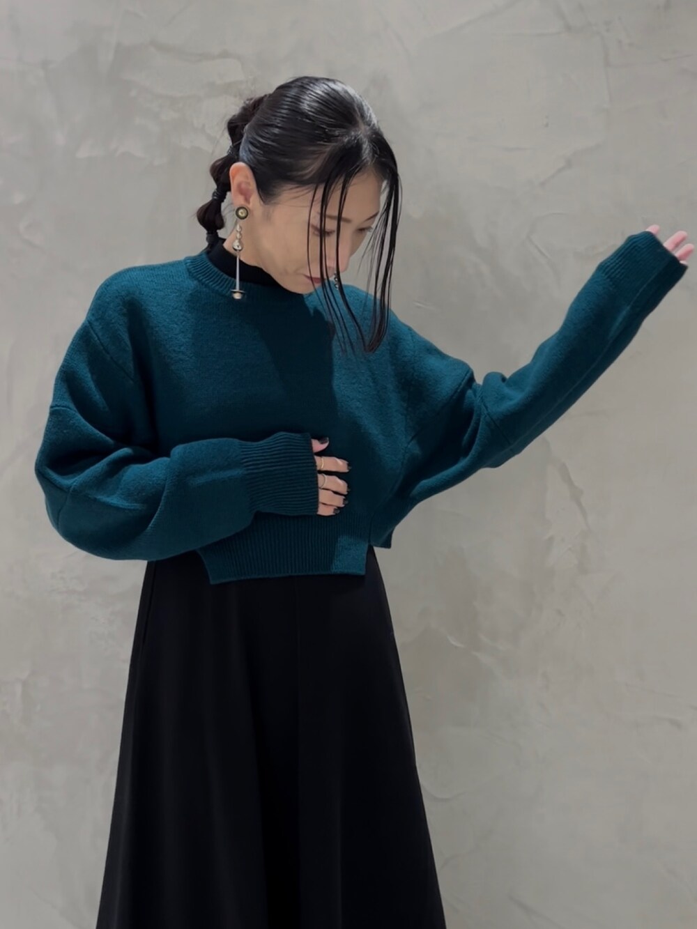 グリーン系のニット/セーター、ブラック系のワンピース、ブラック系のブーツを着用したレディースの秋コーディネートの4枚目の写真