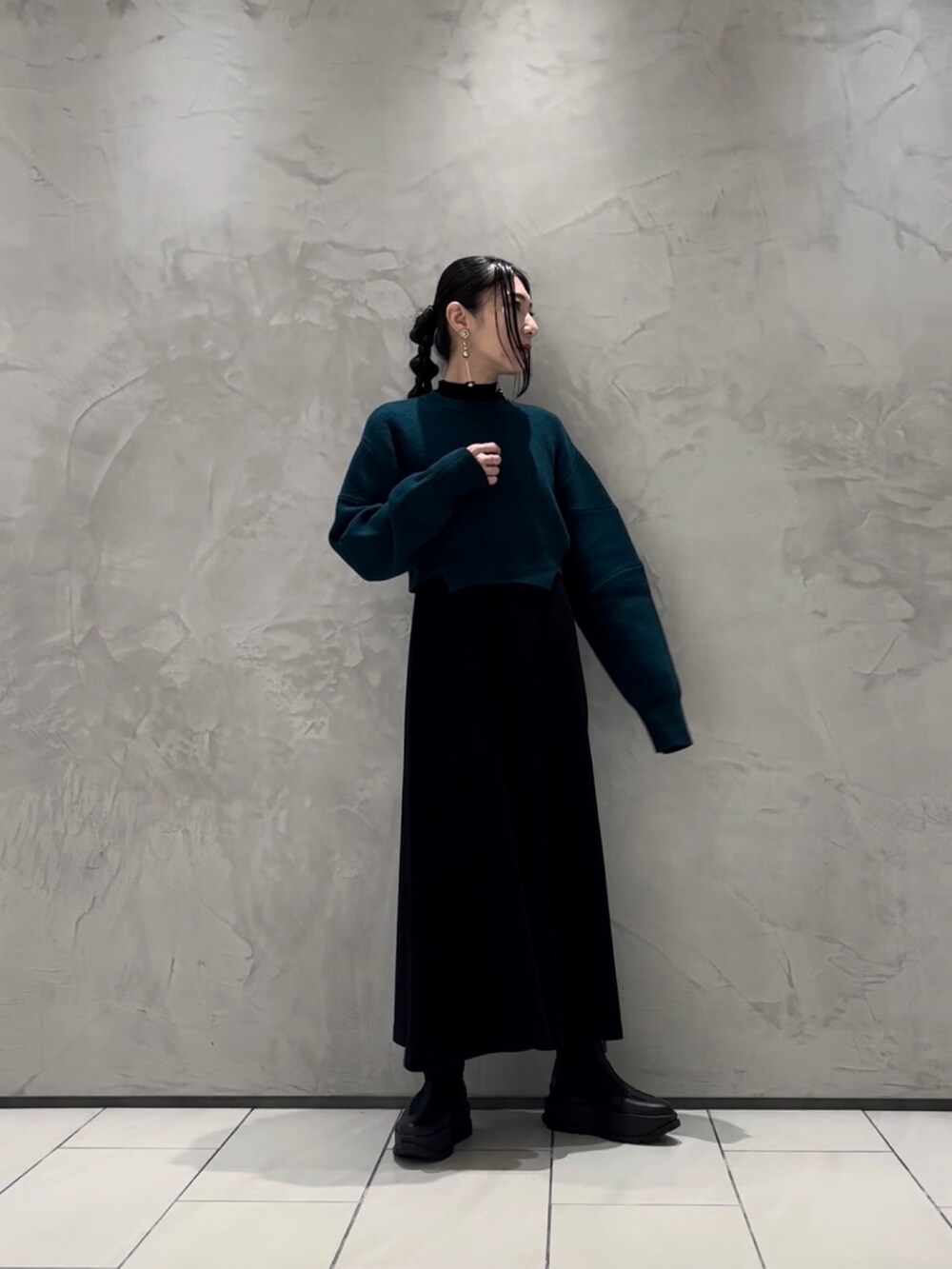 グリーン系のニット/セーター、ブラック系のワンピース、ブラック系のブーツを着用したレディースの秋コーディネートの2枚目の写真