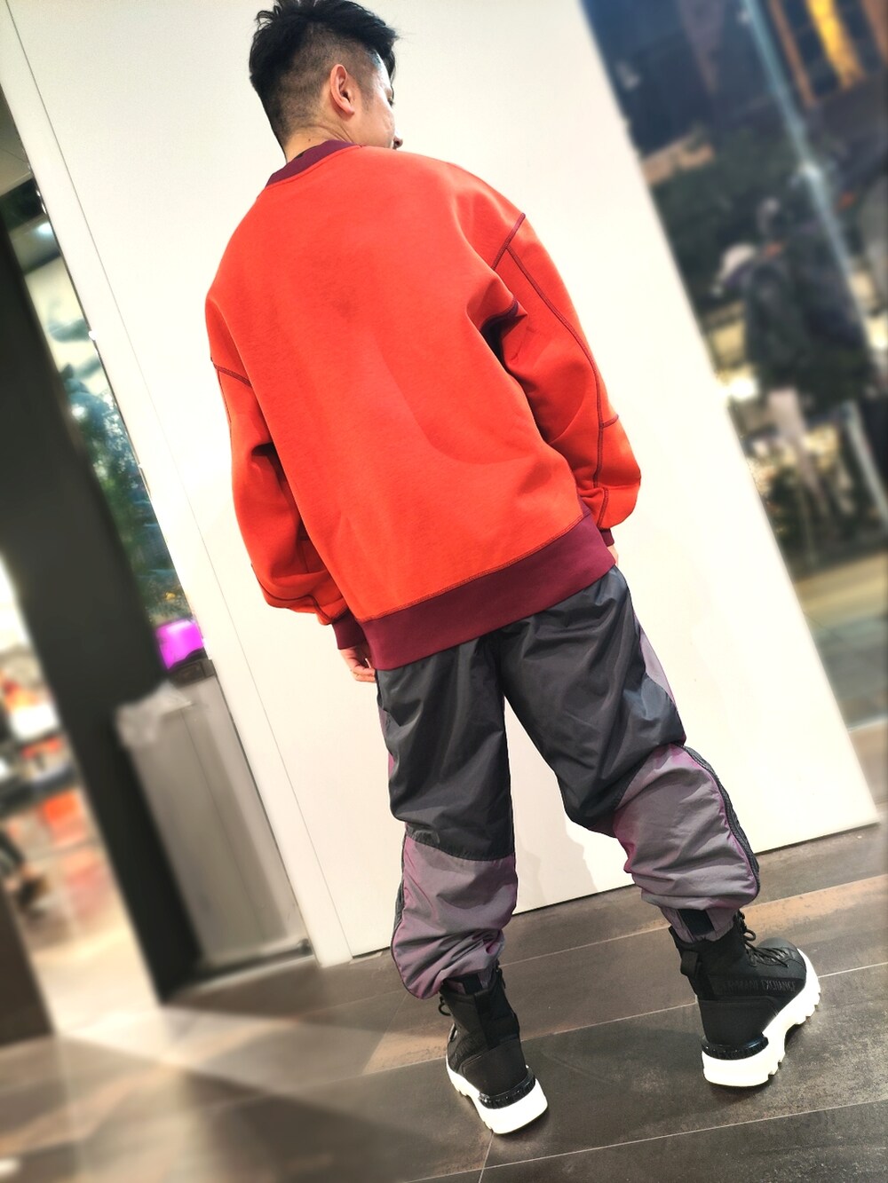 オレンジ系のスウェット、パープル系のチノパンツ、ブラック系のブーツを着用したメンズの秋コーディネートの2枚目の写真