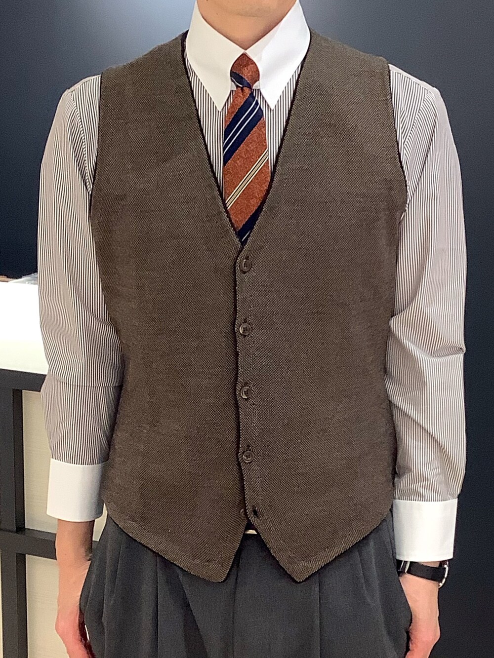 オレンジ系のネクタイ、ブラウン系のビジネスシャツ、ブラウン系のベストを着用したメンズの冬コーディネートの2枚目の写真