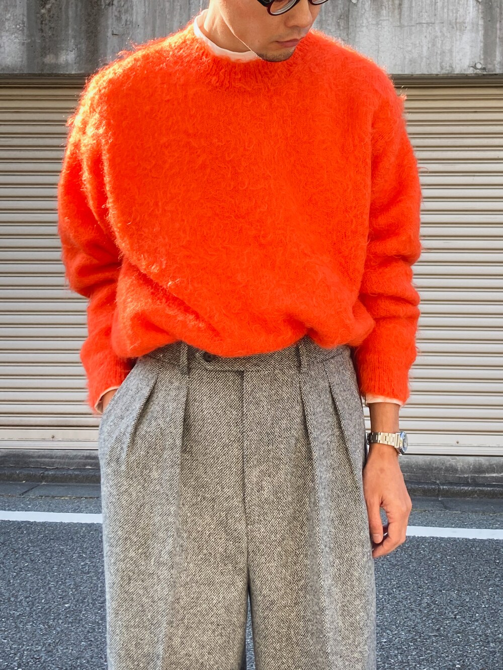 オレンジ系のニット/セーター、グレー系のスラックス、ブラック系のスニーカーを着用したメンズの秋コーディネートの3枚目の写真