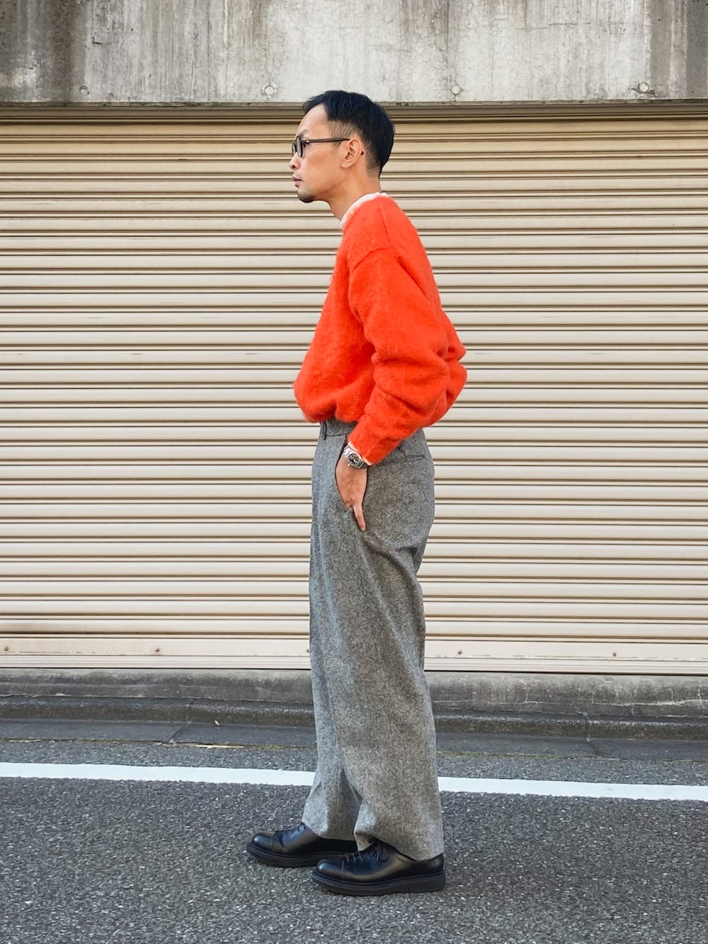 オレンジ系のニット/セーター、グレー系のスラックス、ブラック系のスニーカーを着用したメンズの秋コーディネートの2枚目の写真