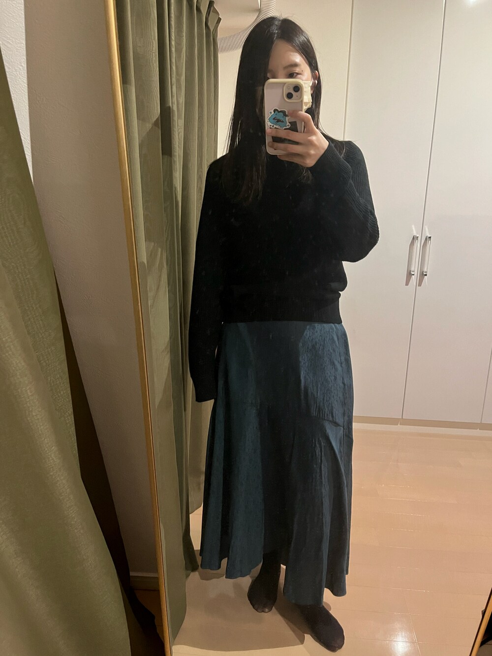 グリーン系のスカート、ブラック系のトップスを着用したレディースの冬コーディネートの2枚目の写真