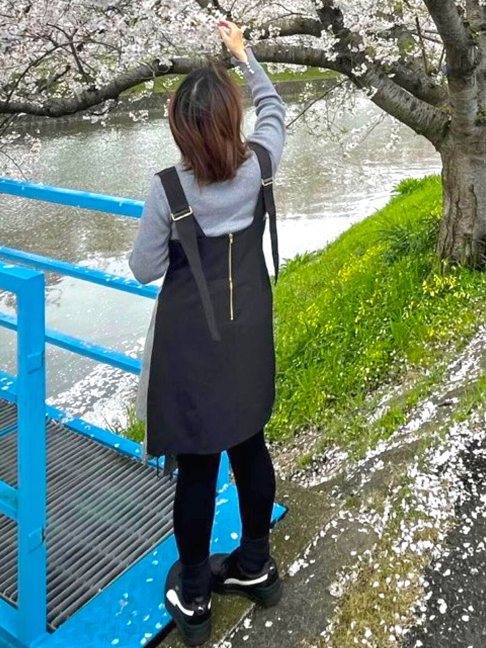 グレー系のニット/セーター、ブラック系のジャンパースカート、グレー系のダウンジャケット/コートを着用したレディースの春コーディネートの2枚目の写真