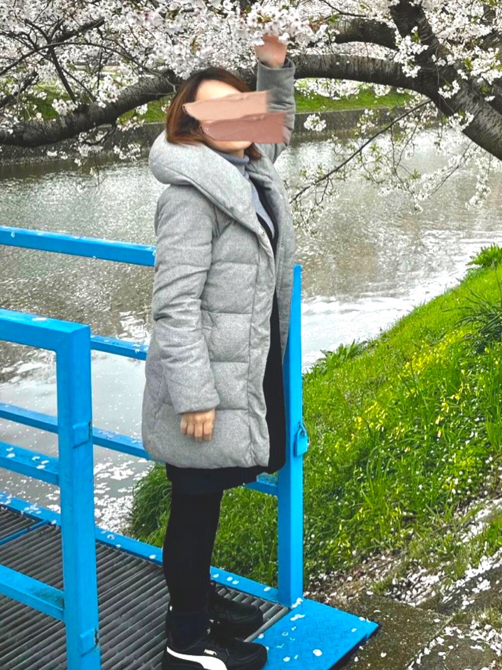 グレー系のニット/セーター、ブラック系のジャンパースカート、グレー系のダウンジャケット/コートを着用したレディースの春コーディネートの3枚目の写真