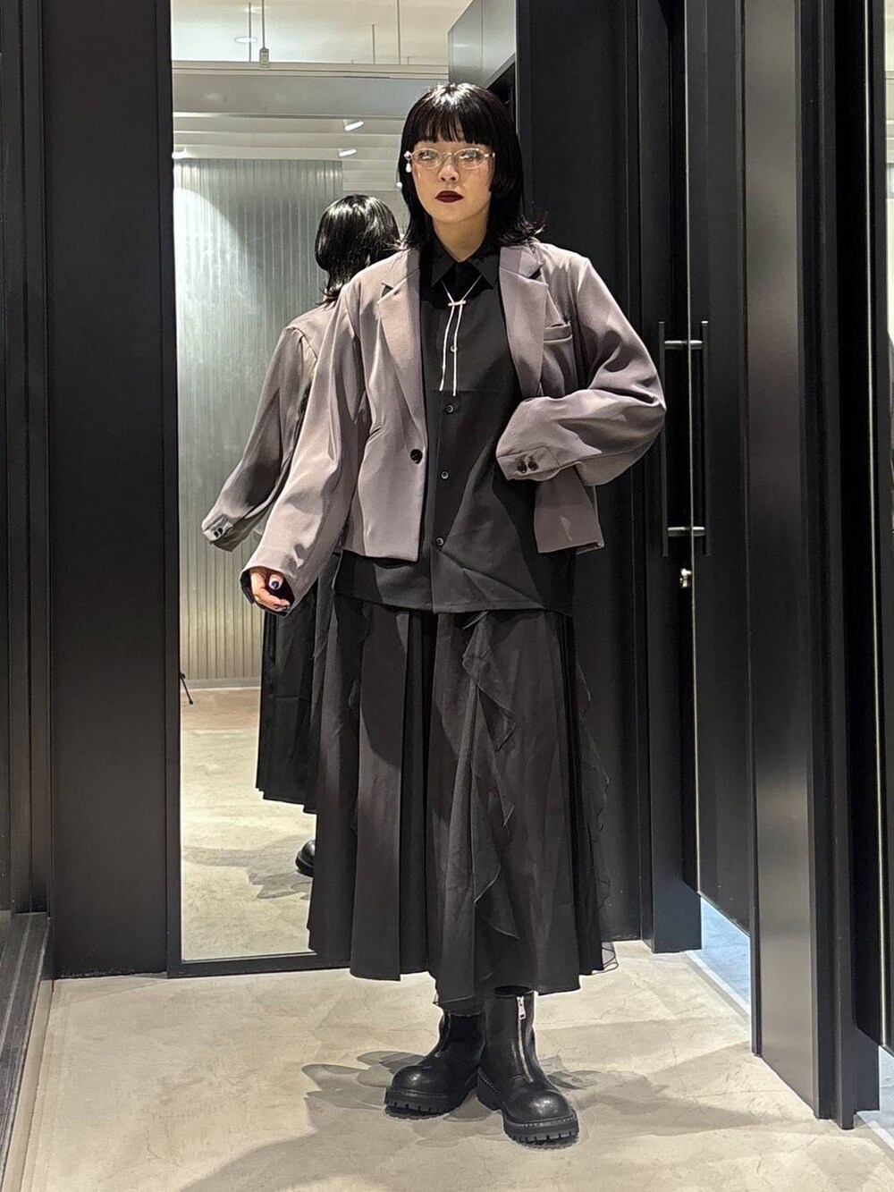 グレー系のテーラードジャケット、ブラック系のスカート、ブラック系のブーツを着用したレディースの秋コーディネートの2枚目の写真