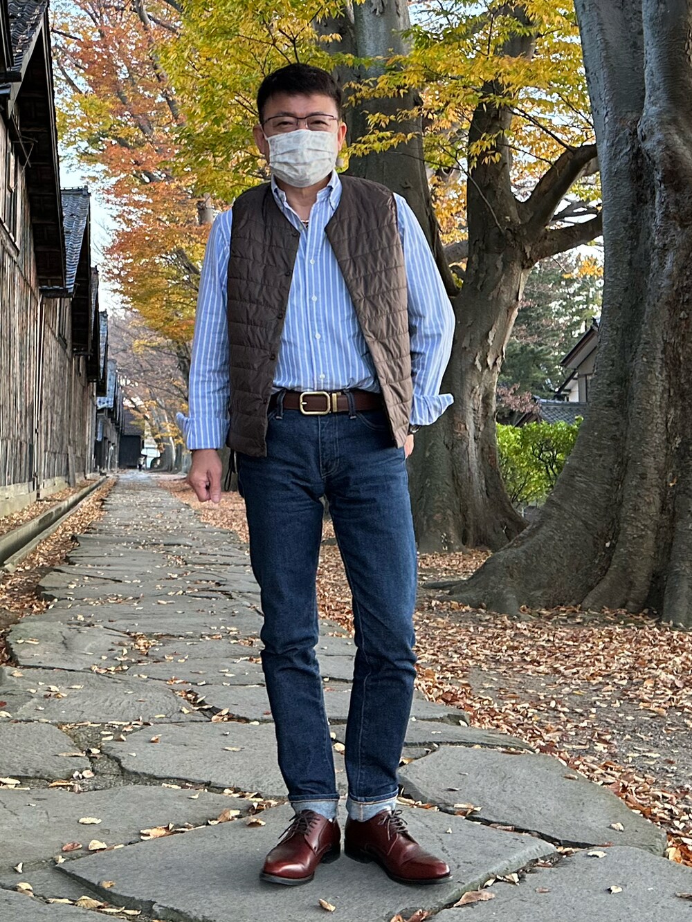 ブルー系のデニムパンツ、ブラック系のナイロンジャケット、ブラウン系のダウンベストを着用したメンズの秋コーディネートの2枚目の写真