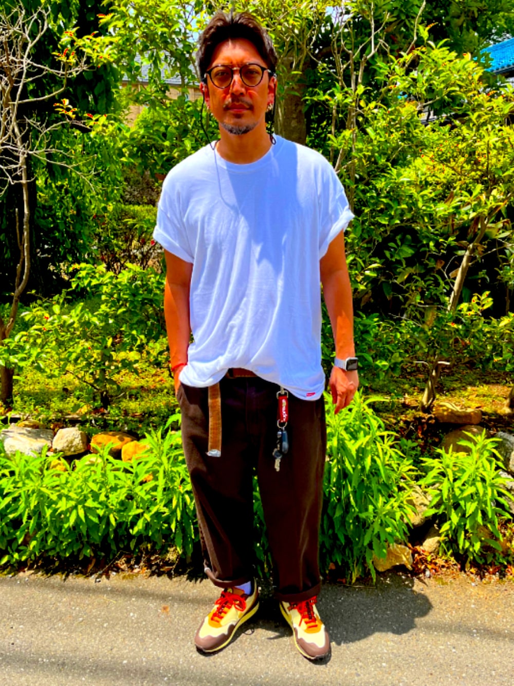 ホワイト系のTシャツ/カットソー、レッド系のチノパンツ、ブラウン系のスニーカーを着用したメンズの夏コーディネートの2枚目の写真