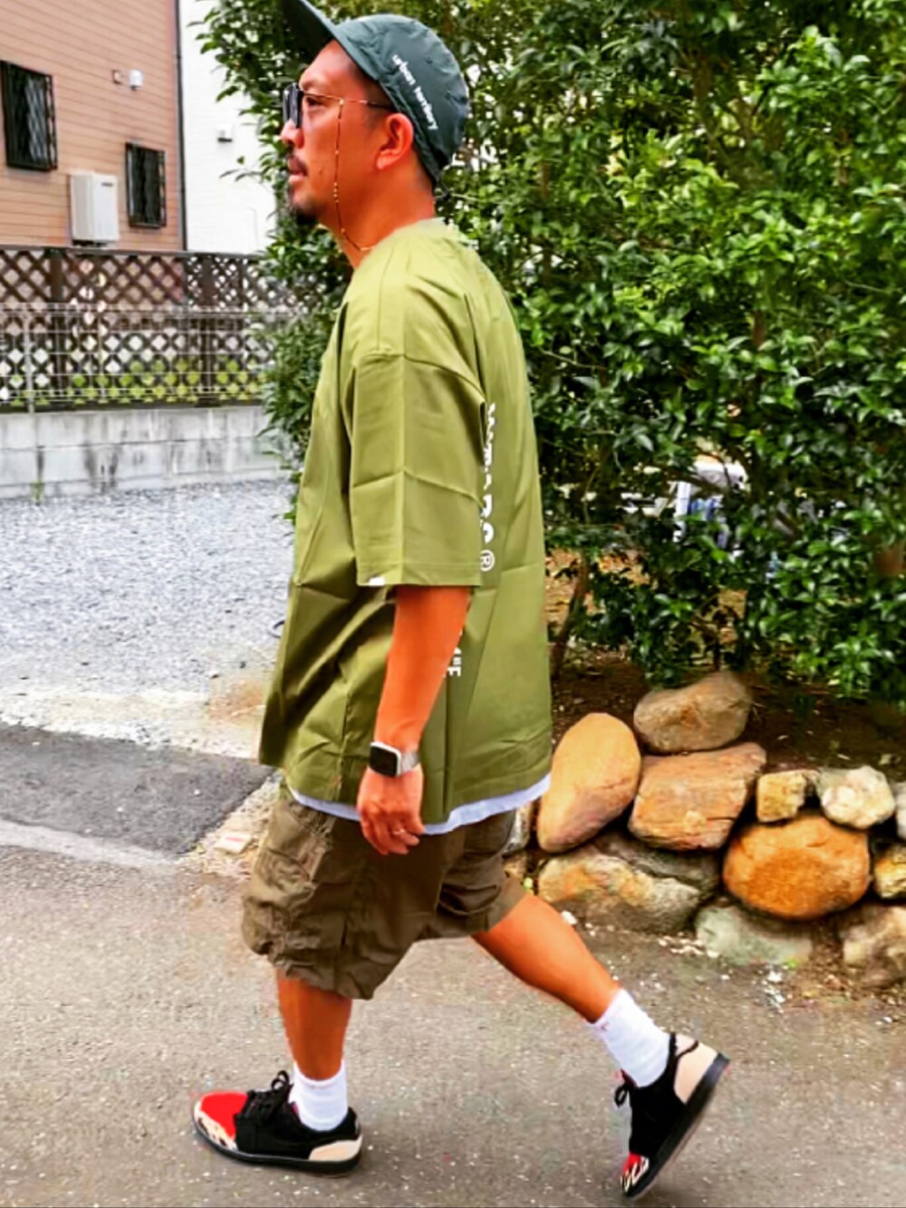 グリーン系のTシャツ/カットソー、ブラック系のパンツ、ブラック系のスニーカーを着用したメンズの夏コーディネートの4枚目の写真