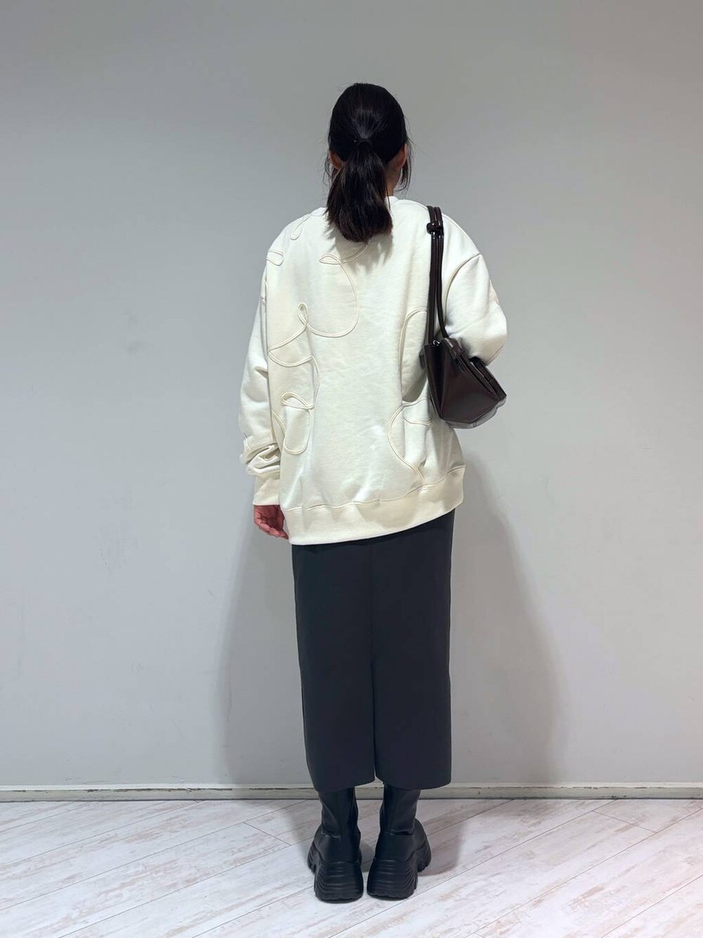 グレー系のスカート、ブラウン系のショルダーバッグ、ブラック系のブーツを着用したレディースの冬コーディネートの3枚目の写真