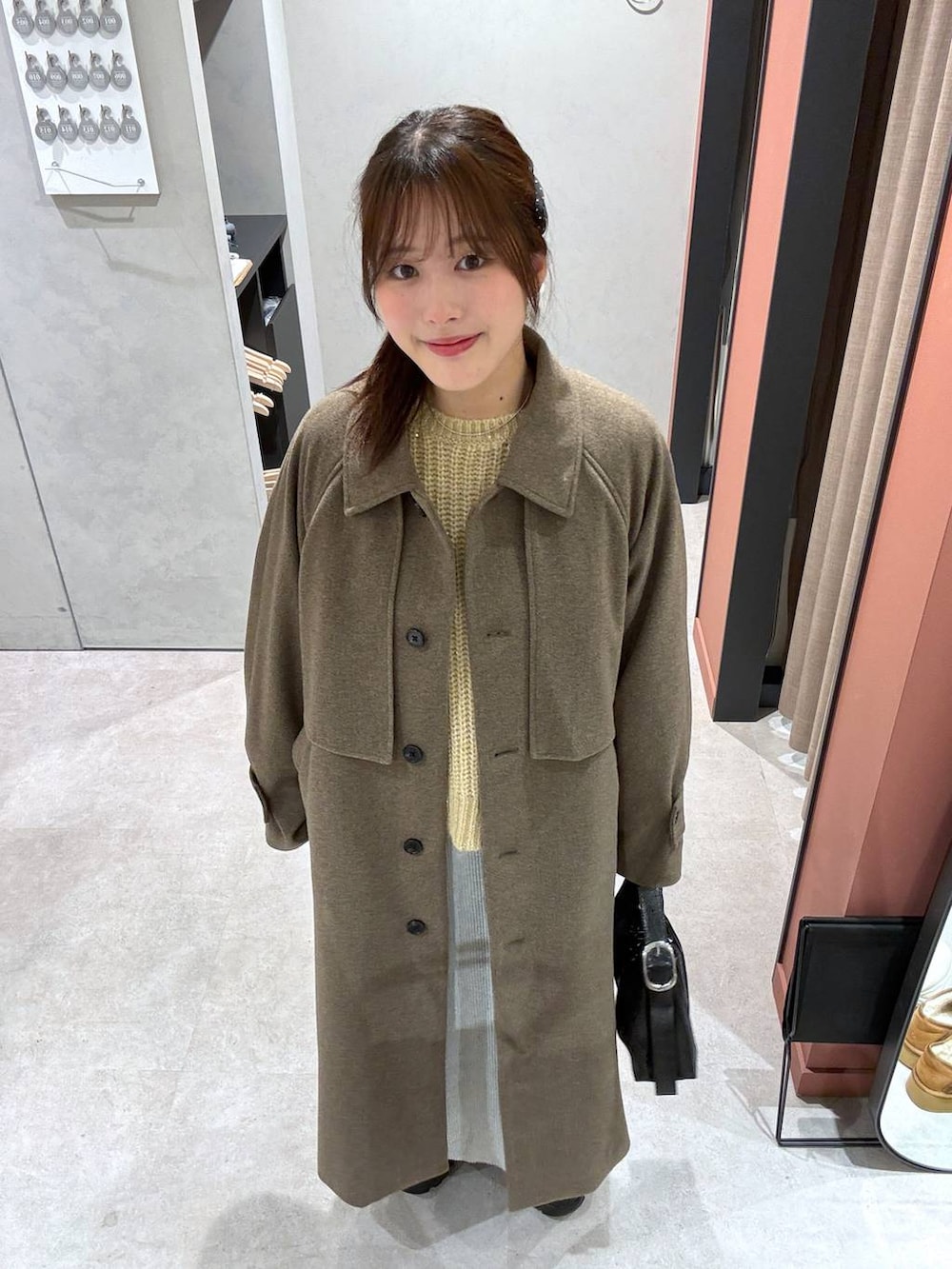 グレー系のスカート、ブラウン系のステンカラーコート、ブラック系のショルダーバッグを着用したレディースの冬コーディネートの4枚目の写真