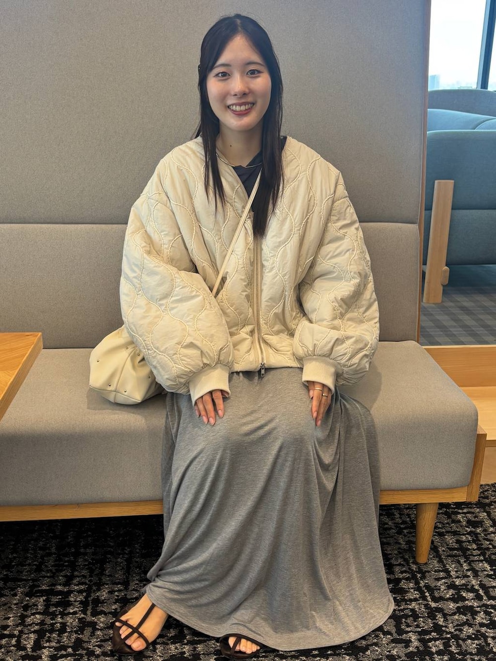 ブラウン系のサンダル、グレー系のスカート、ホワイト系のブルゾンを着用したレディースの秋コーディネートの3枚目の写真