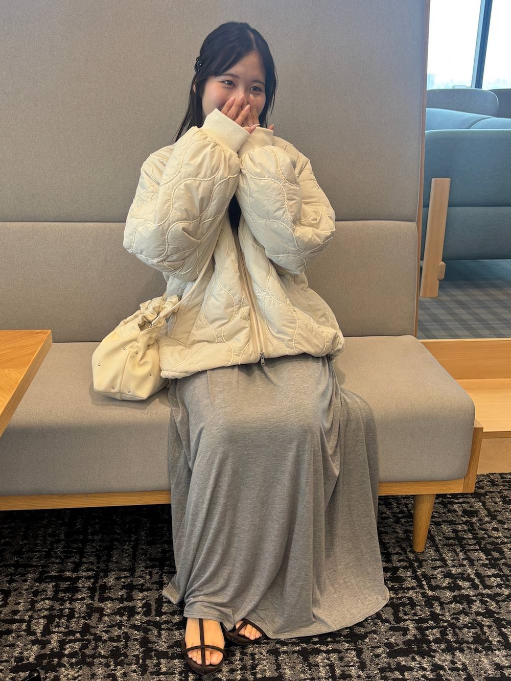 ブラウン系のサンダル、グレー系のスカート、ホワイト系のブルゾンを着用したレディースの秋コーディネートの2枚目の写真