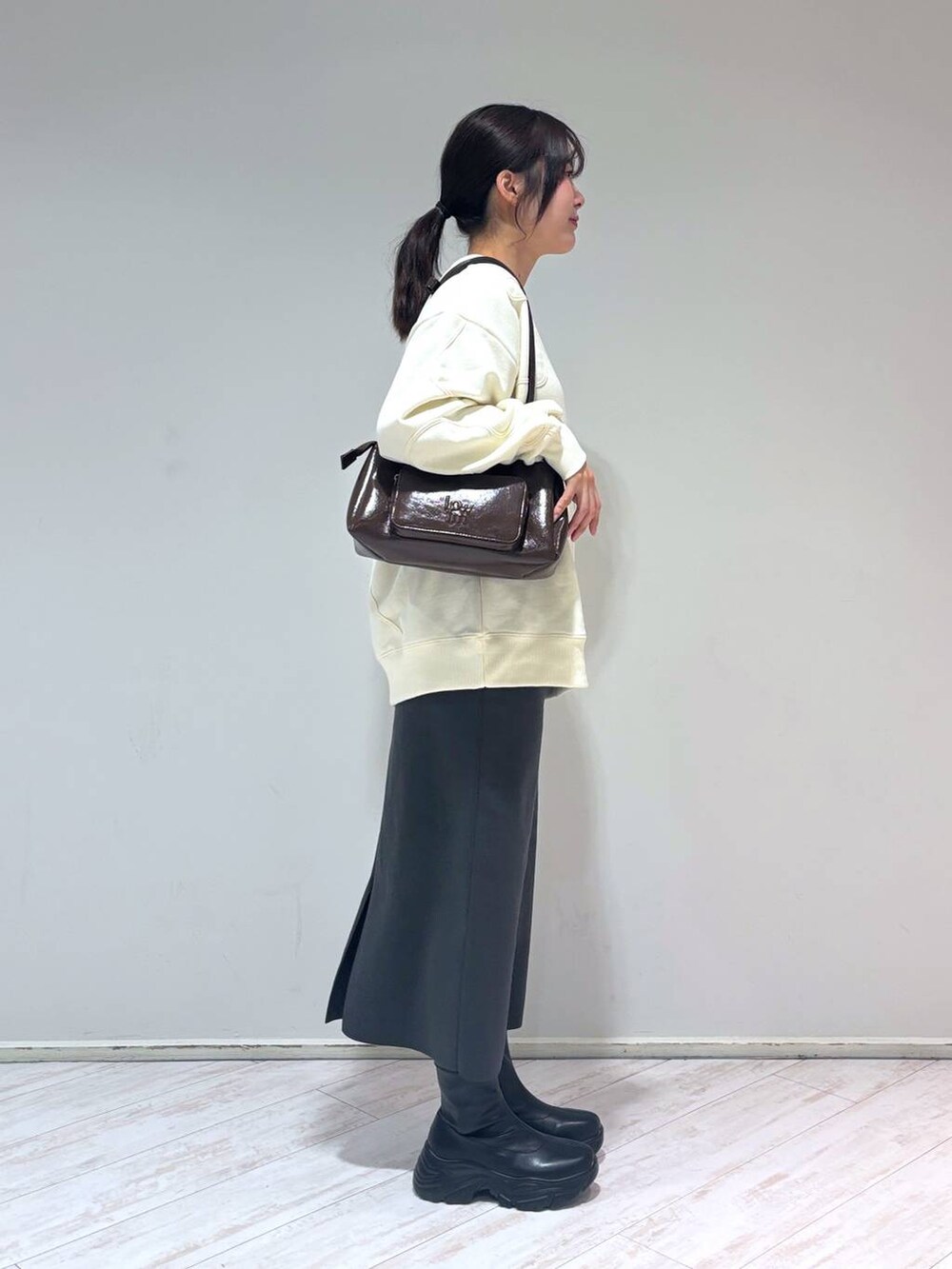 グレー系のスカート、ブラウン系のショルダーバッグ、ブラック系のブーツを着用したレディースの冬コーディネートの2枚目の写真