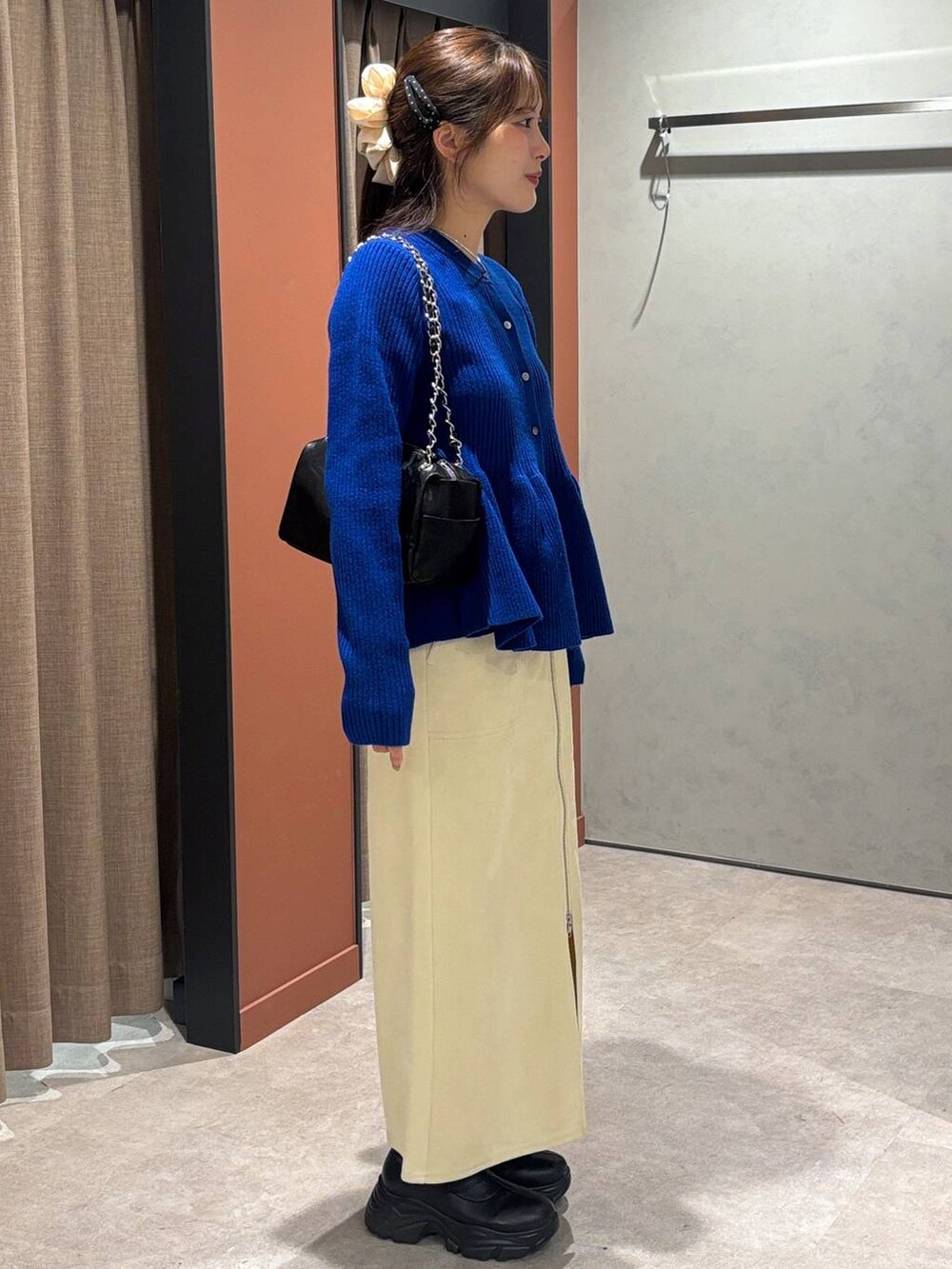 ブラック系のブーツ、ホワイト系のスカート、ブルー系のカーディガン/ボレロを着用したレディースの秋コーディネートの2枚目の写真