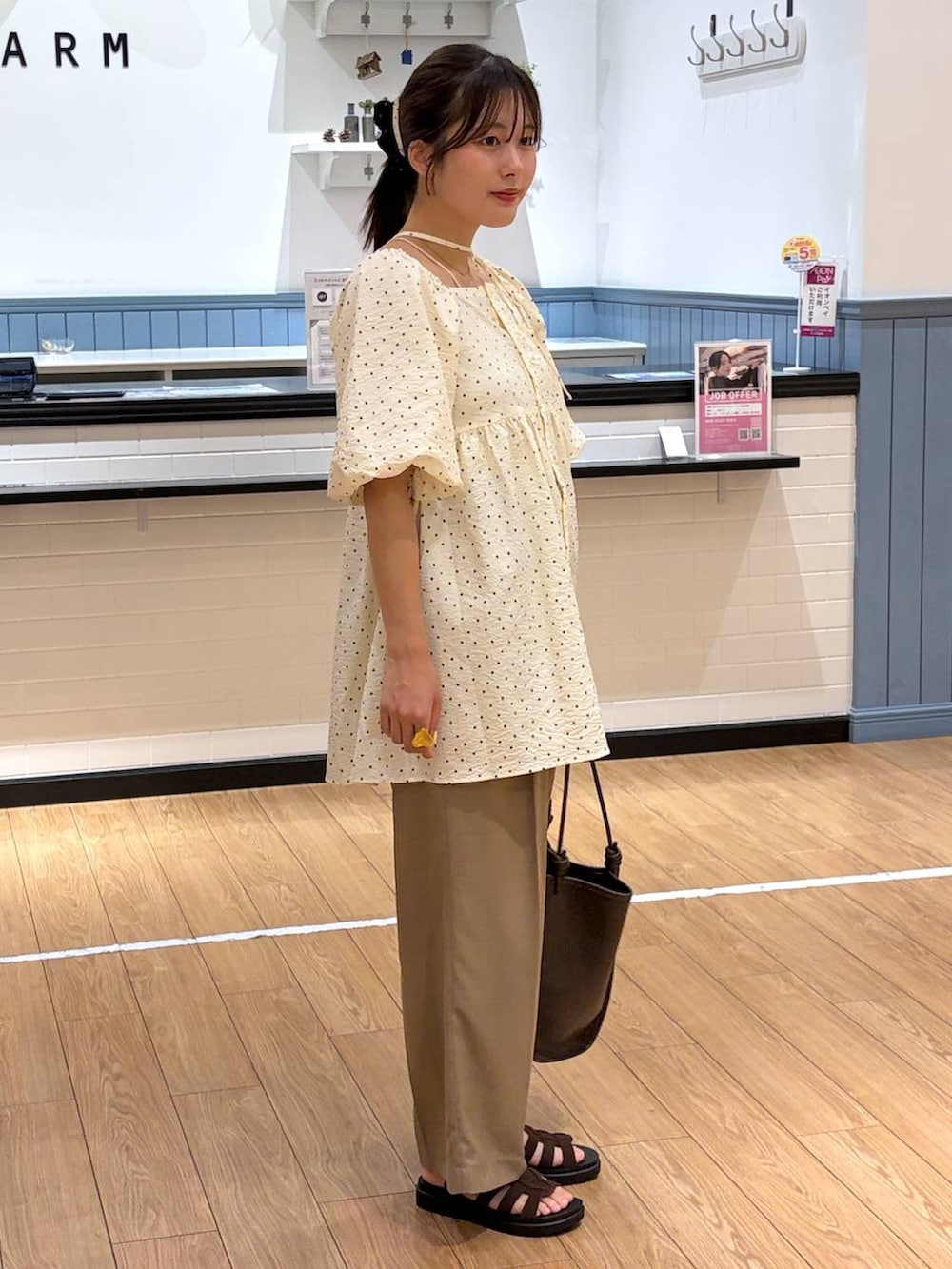 ベージュ系のスラックス、ブラウン系のサンダル、ブラウン系のトートバッグを着用したレディースの夏コーディネートの2枚目の写真