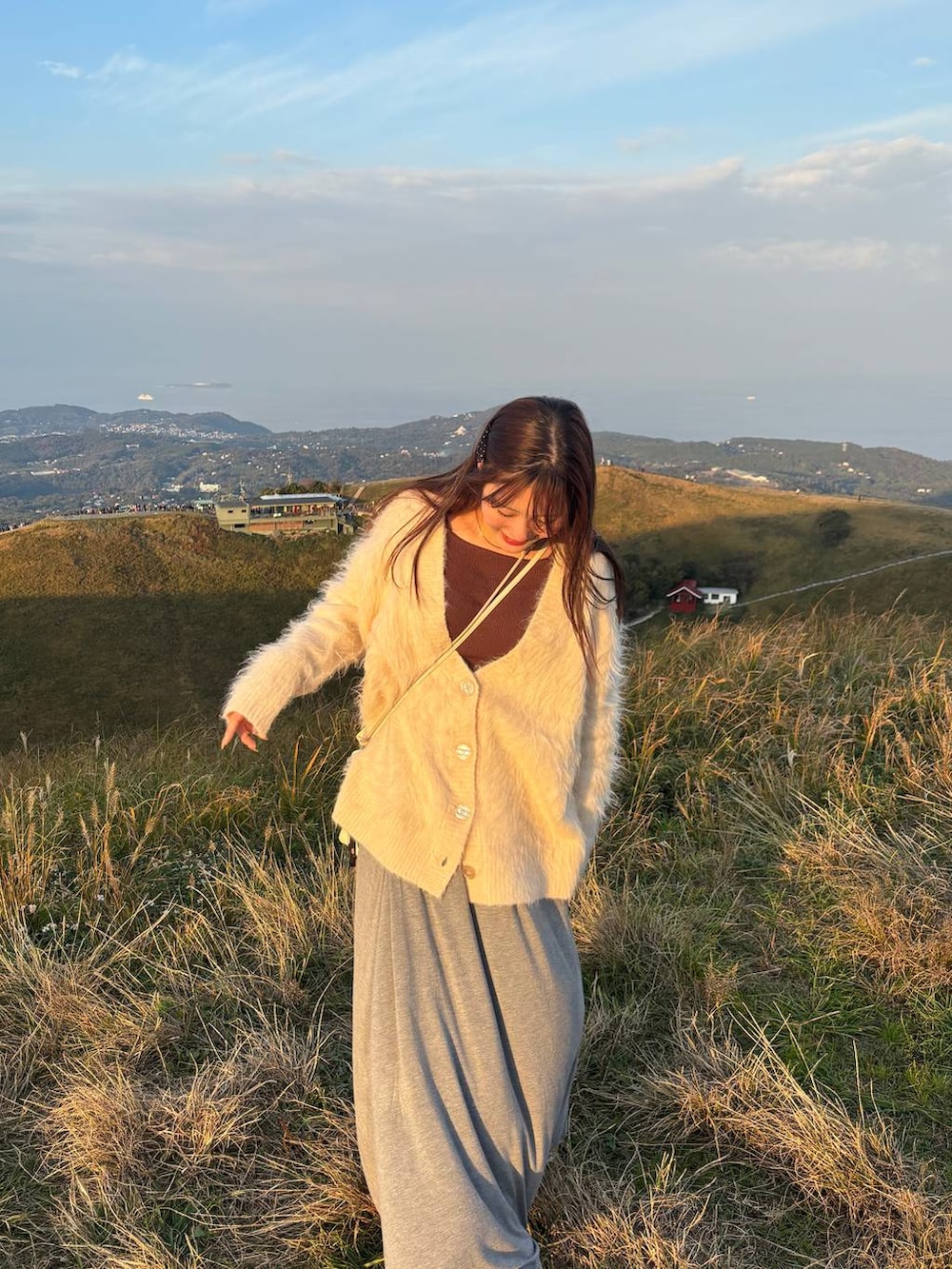 グレー系のスカート、ブラウン系のニット/セーター、ホワイト系のカーディガン/ボレロを着用したレディースの秋コーディネートの2枚目の写真