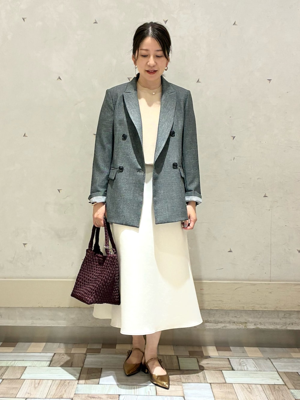 グレー系のテーラードジャケット、ホワイト系のスカート、イエロー系のニット/セーターを着用したレディースの秋コーディネートの2枚目の写真