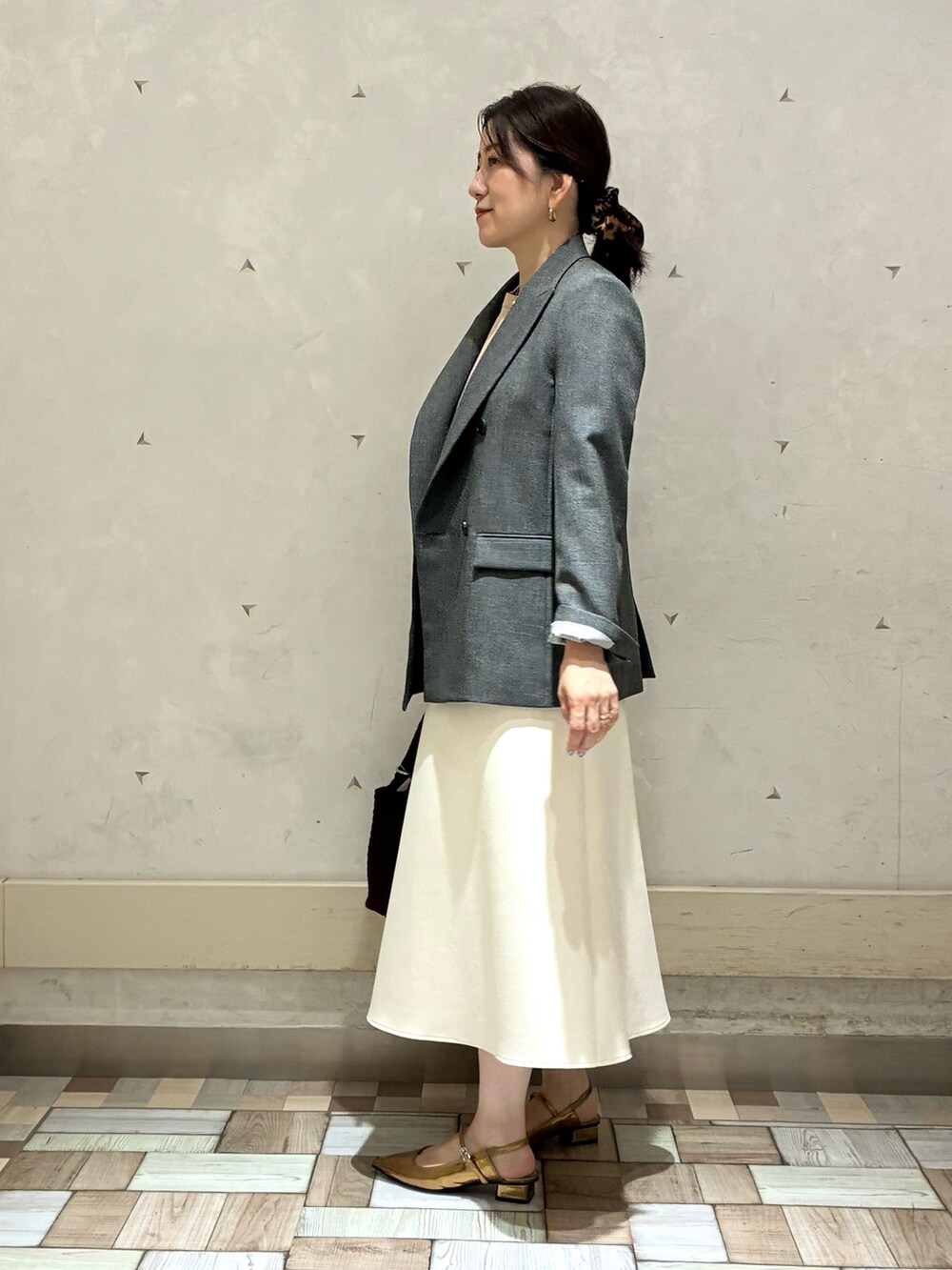 グレー系のテーラードジャケット、ホワイト系のスカート、イエロー系のニット/セーターを着用したレディースの秋コーディネートの3枚目の写真