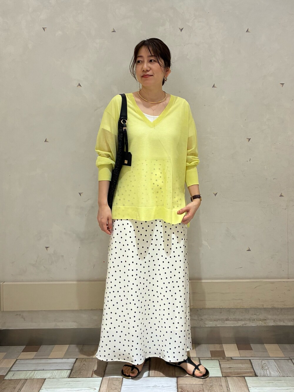 ホワイト系のスカート、イエロー系のニット/セーター、ブラック系のショルダーバッグを着用したレディースの春コーディネートの2枚目の写真