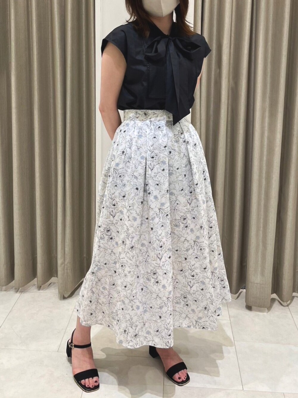 ブラック系のシャツ/ブラウス、ホワイト系のスカート、ブラック系のサンダルを着用したレディースの夏コーディネートの2枚目の写真