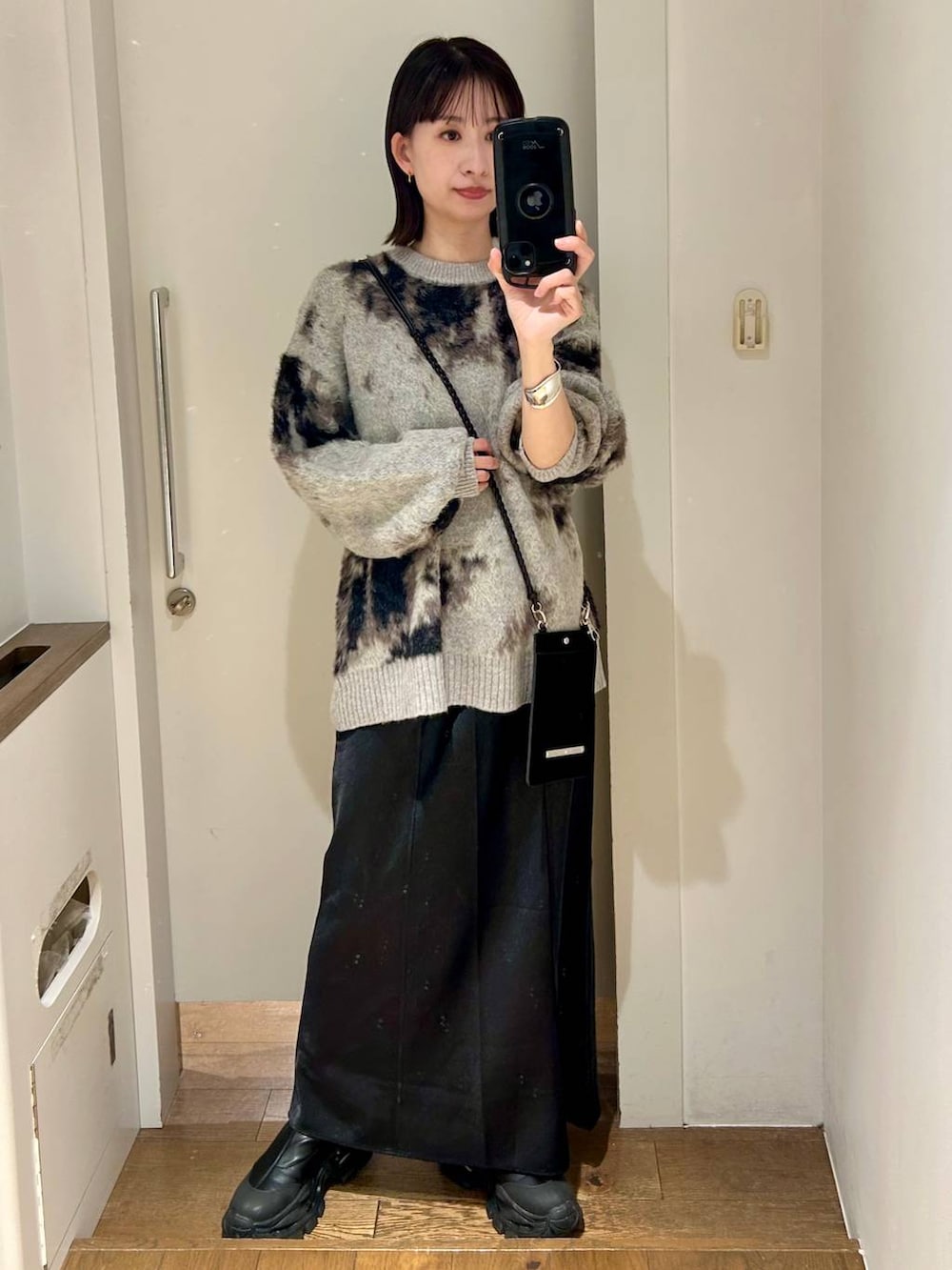 グレー系のニット/セーター、ブラック系のブーツ、ブラック系のスカートを着用したレディースの秋コーディネートの3枚目の写真