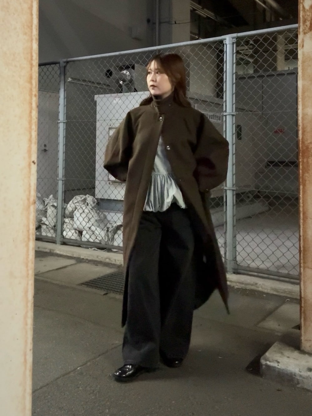 ブラウン系のステンカラーコート、グリーン系のTシャツ/カットソー、ブラック系のデニムパンツを着用したレディースの秋コーディネートの2枚目の写真