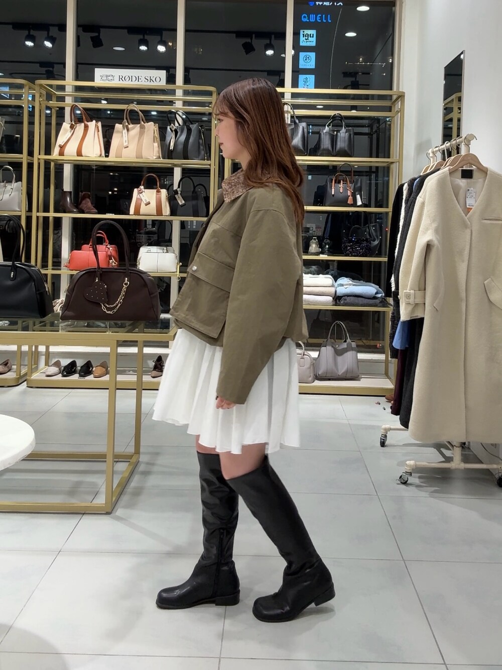 グリーン系のブルゾン、ホワイト系のワンピース、ブラック系のブーツを着用したレディースの冬コーディネートの2枚目の写真