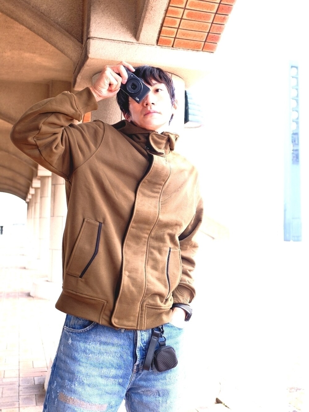 ブラウン系のパーカー、ブルー系のデニムパンツ、ブラック系のボディバッグ/ウエストポーチを着用したメンズの秋コーディネートの2枚目の写真