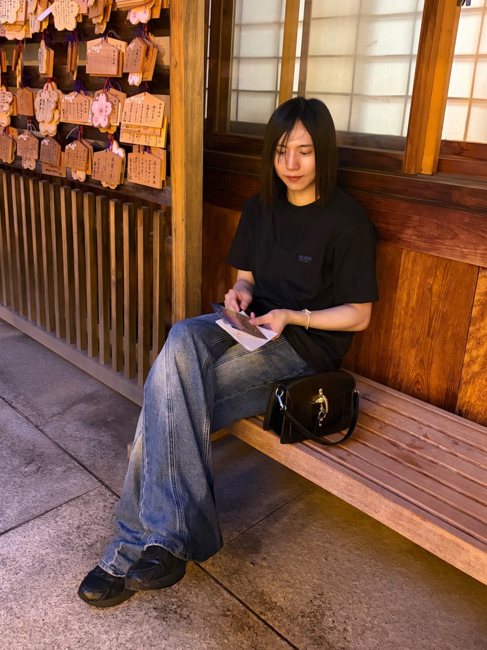ブラック系のハンドバッグ、ブラック系のTシャツ/カットソー、ブルー系のデニムパンツを着用したメンズの夏コーディネートの2枚目の写真