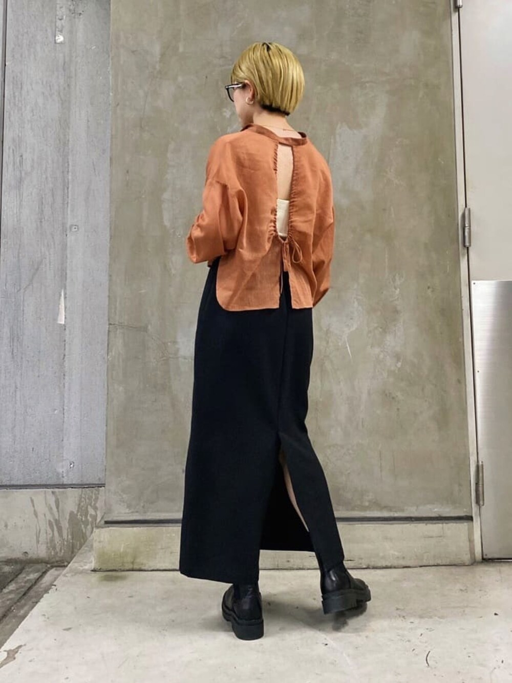 ブラック系のスカート、オレンジ系のシャツ/ブラウス、ブラック系のブーツを着用したレディースの秋コーディネートの2枚目の写真