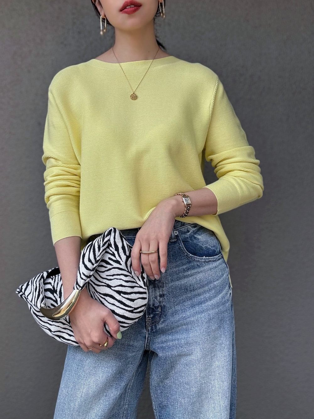 イエロー系のニット/セーター、ブルー系のデニムパンツ、ゴールド系のパンプスを着用したレディースの春コーディネートの2枚目の写真