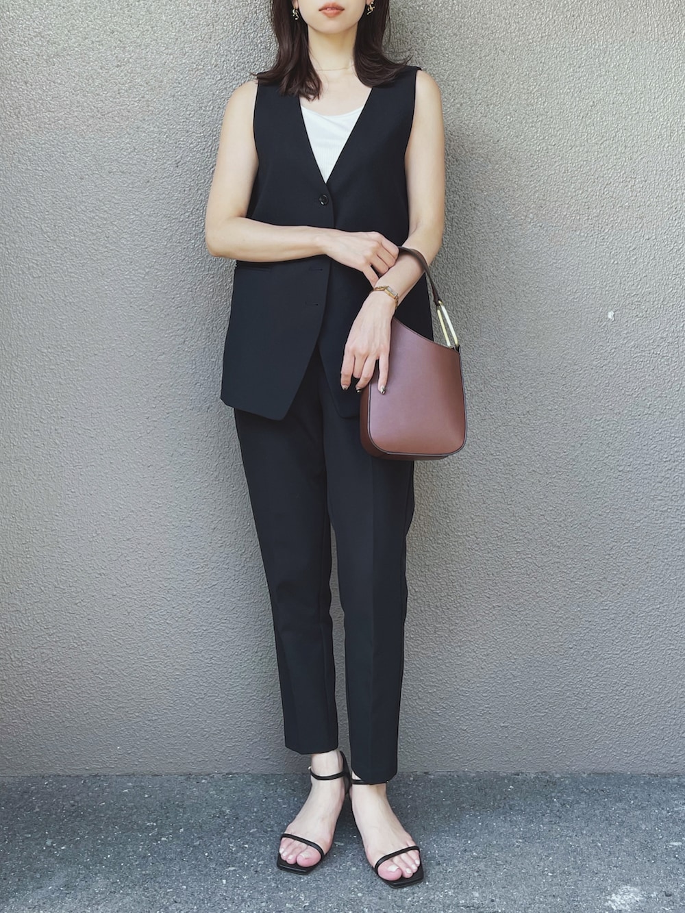 ブラック系のベスト、ブラウン系のハンドバッグ、ブラック系のサンダルを着用したレディースの夏コーディネートの2枚目の写真