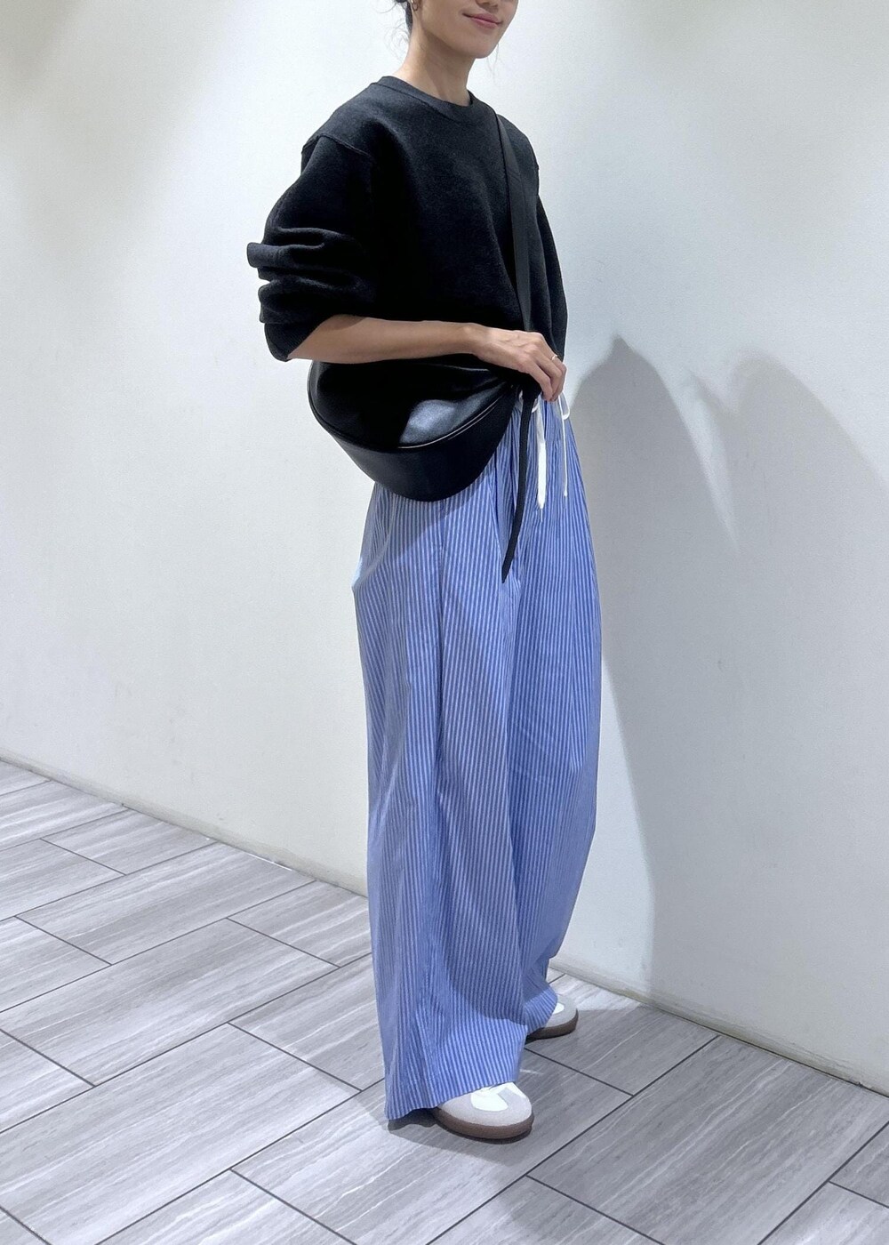 ブラック系のショルダーバッグ、ブルー系のスラックス、ホワイト系のスニーカーを着用したレディースの秋コーディネートの2枚目の写真