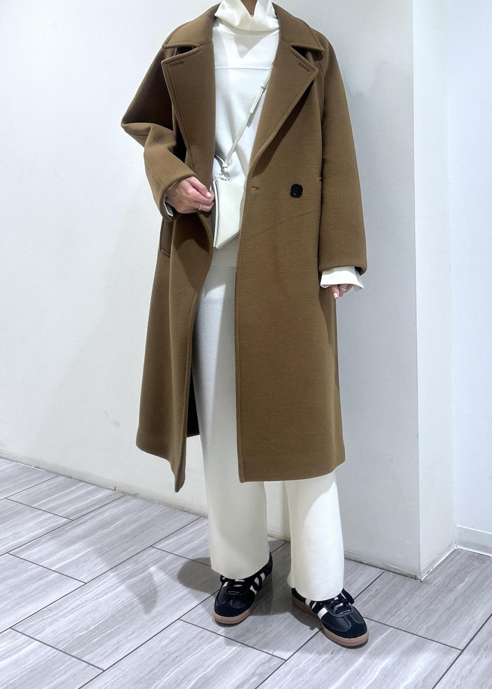 イエロー系のステンカラーコート、ホワイト系のニット/セーター、ホワイト系のその他パンツを着用したレディースの秋コーディネートの2枚目の写真