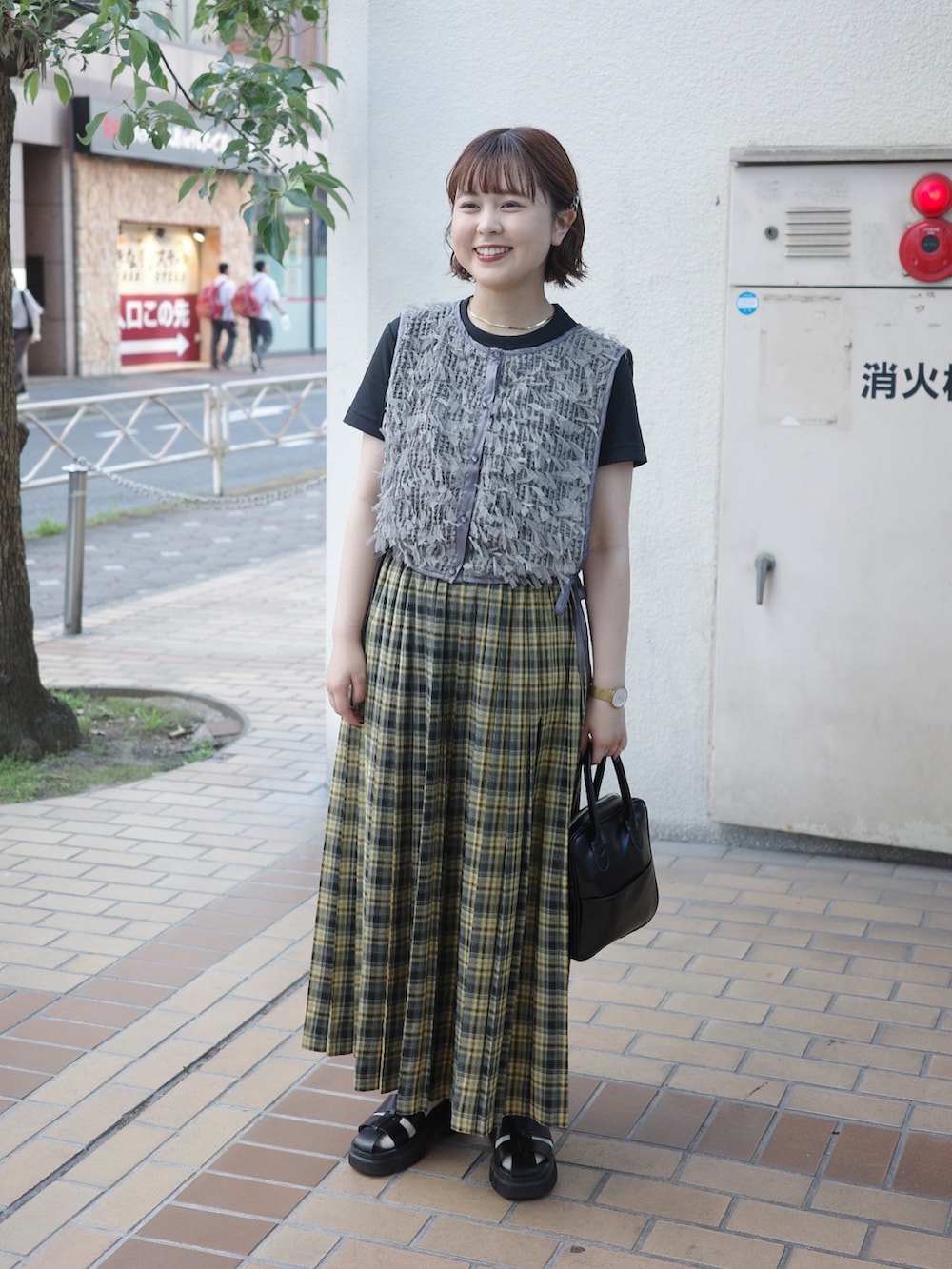 イエロー系のスカート、グレー系のベスト、ブラック系のサンダルを着用したレディースの夏コーディネートの2枚目の写真