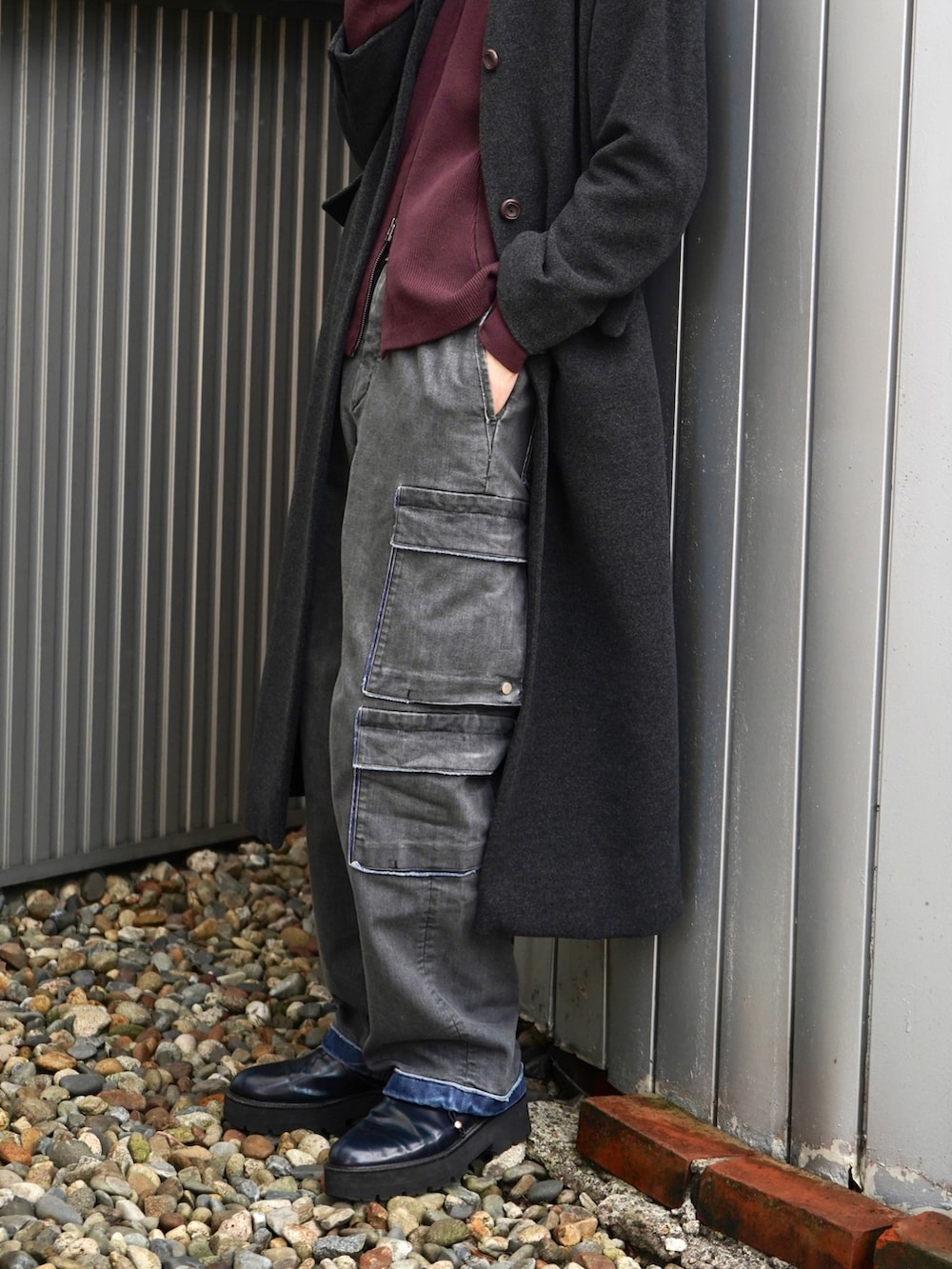 レッド系のニット/セーター、グレー系のノーカラーコート、ブラック系のデニムパンツを着用したメンズの秋コーディネートの2枚目の写真