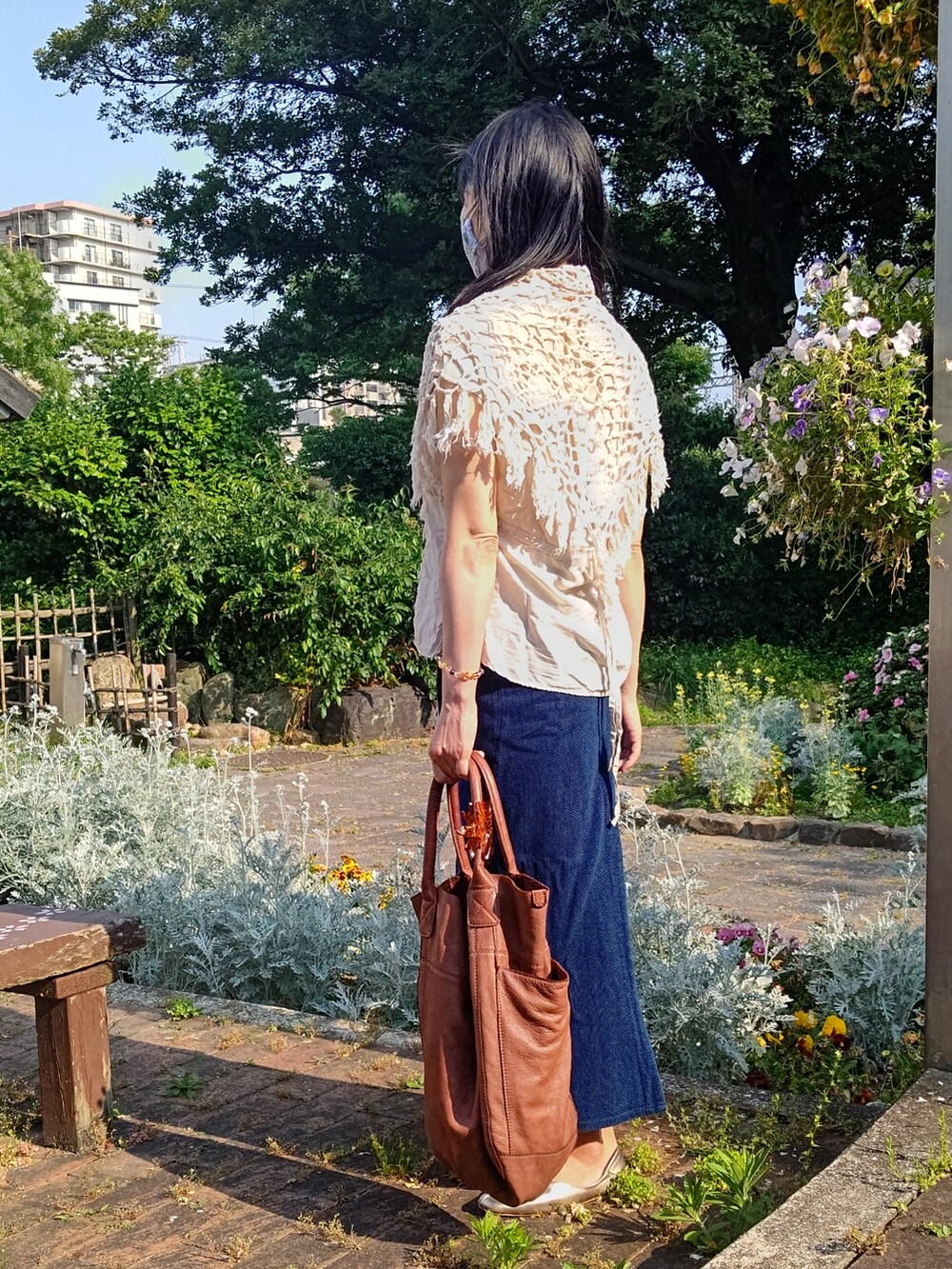 ゴールド系のスリッポン、ブラウン系のトートバッグ、ブルー系のデニムスカートを着用したレディースの春コーディネートの2枚目の写真