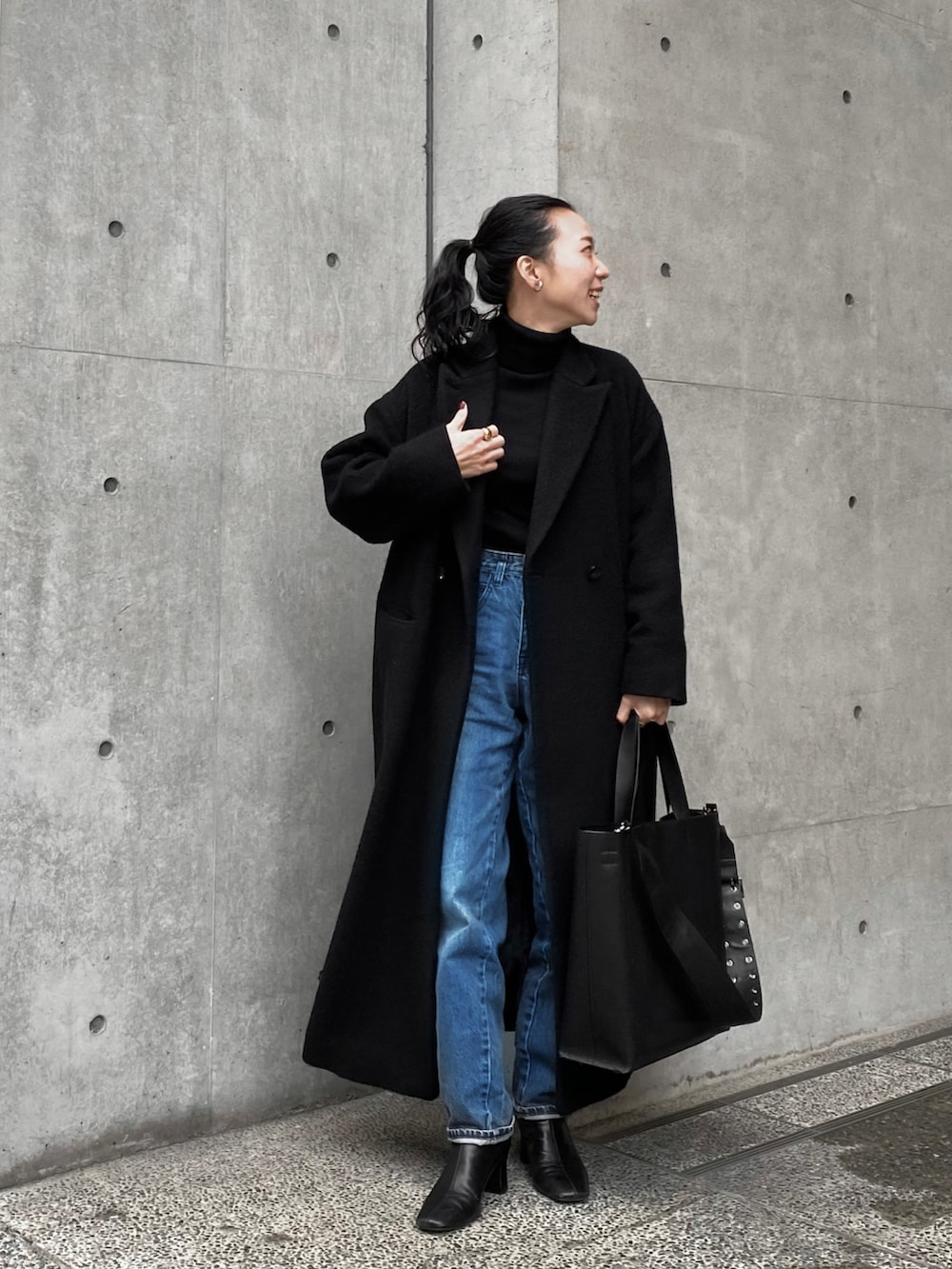 ブラック系のチェスターコート、ブラック系のトートバッグ、ブルー系のデニムパンツを着用したレディースの冬コーディネートの2枚目の写真