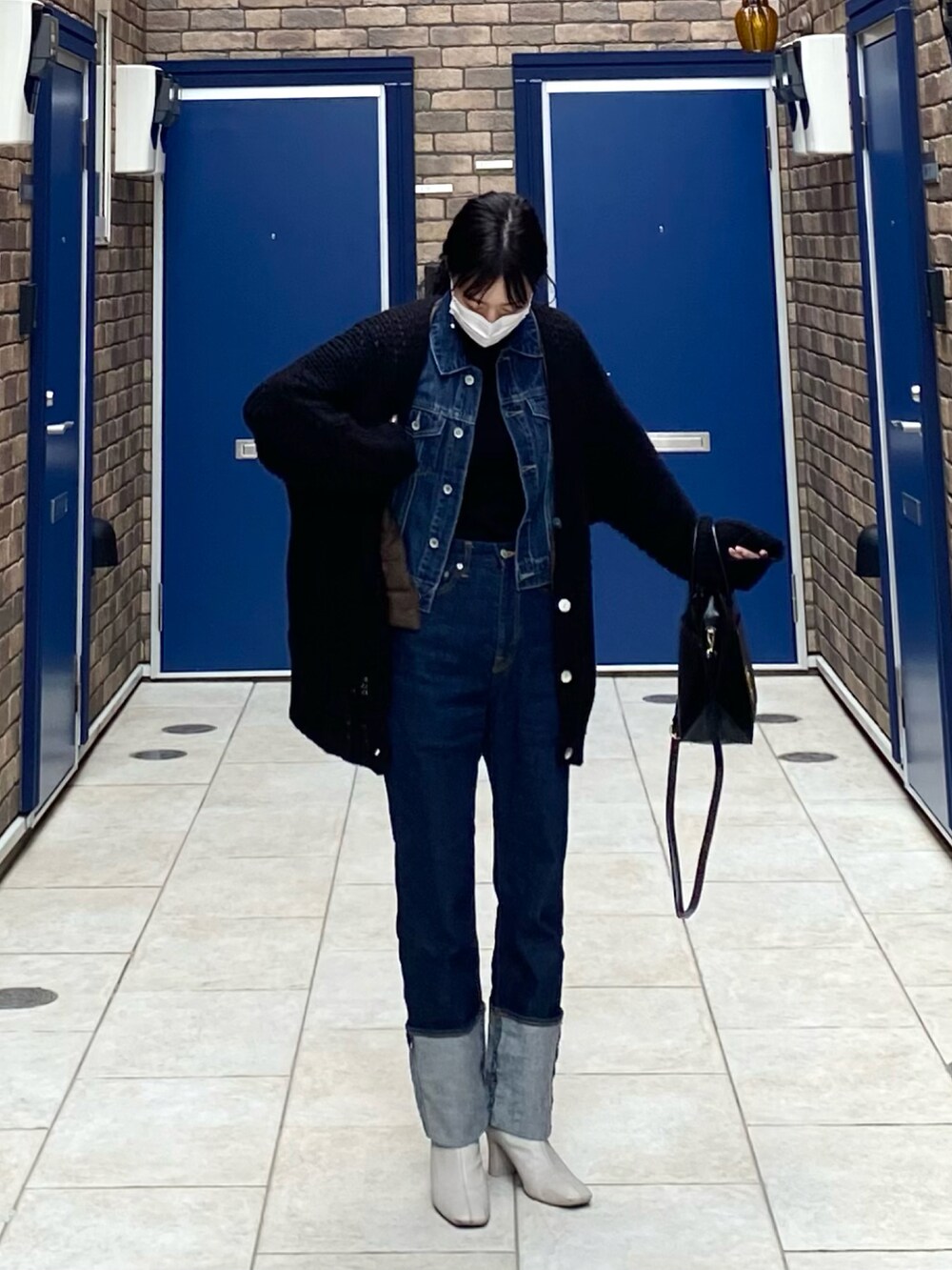 ブラック系のショルダーバッグ、ブラック系のブーツ、ブルー系のデニムパンツを着用したレディースの春コーディネートの2枚目の写真