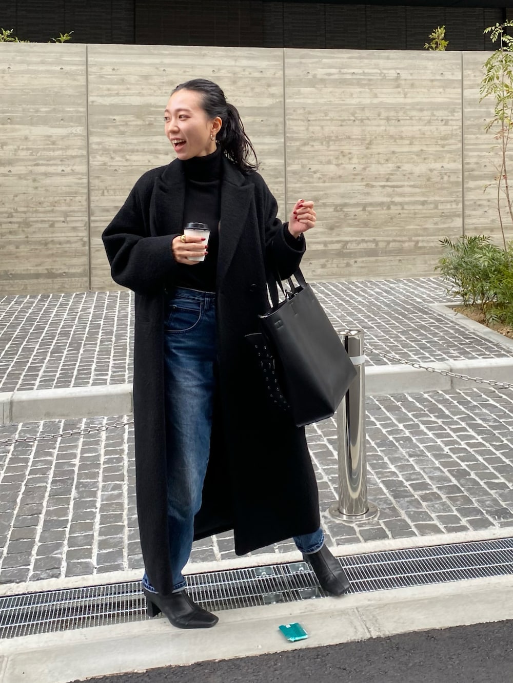 ブラック系のチェスターコート、ブラック系のトートバッグ、ブルー系のデニムパンツを着用したレディースの冬コーディネートの3枚目の写真