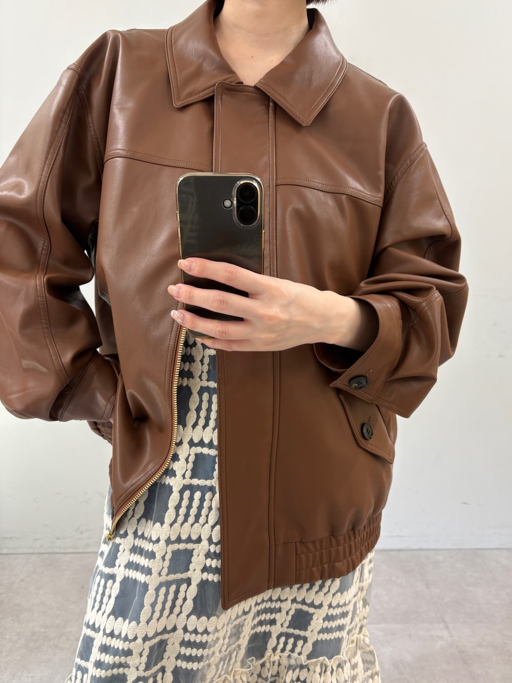 ブラウン系のブルゾン、ホワイト系のワンピース、ブルー系のデニムパンツを着用したレディースの秋コーディネートの2枚目の写真